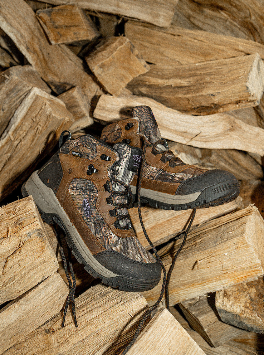 Product shot of Skokie work boots in brown and camo colorway placed on pile of wood logs