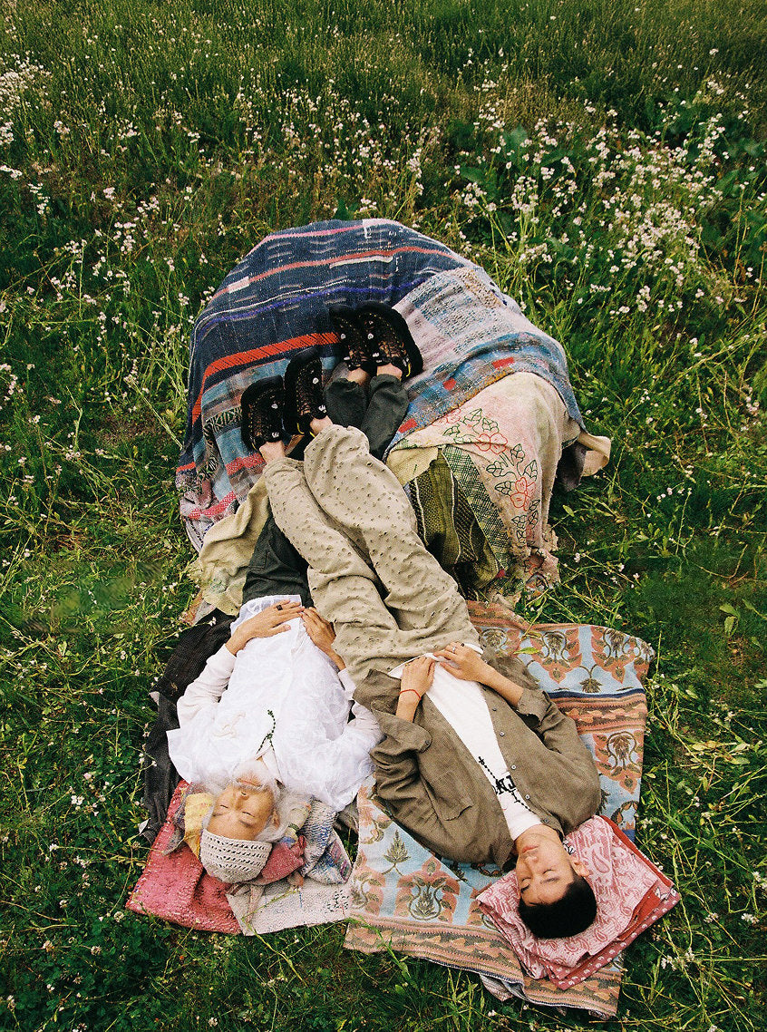 Two men laying on picnic blankets in grassy fields with their feet up on a blanket pile while wearing Keen and FAF collaboration Uneek sandals. 