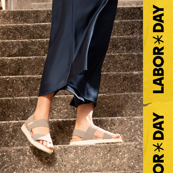 Knee-down shot of woman wearing black satin skirt and Elle backstrap sandals standing on concrete stairs. Embedded text reads "Labor Day" in yellow. 