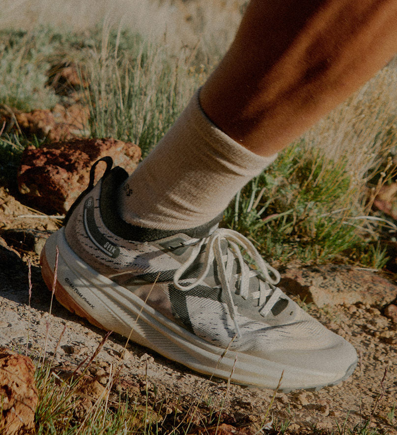 Knee down shot of man in shorts and crew socks wearing tan and black Seek trail running shoe on dirt trail