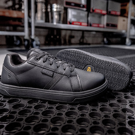 Product shot of black leather, non slip service shoes on kitchen floor mat. 