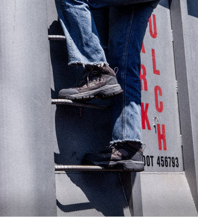 Man wearing blue jeans and work boots while climbing up metal ladder on tower 