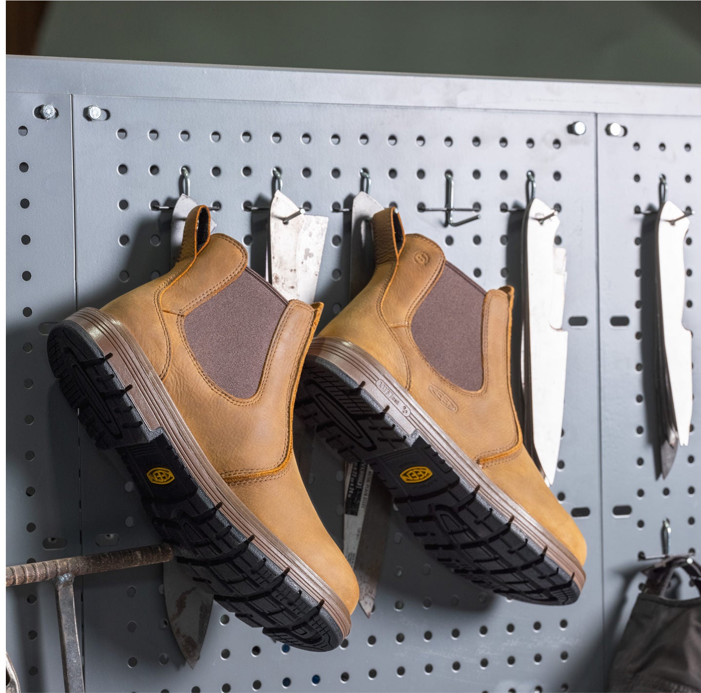  A pair of brown leather, slip-on work boots displayed on a pegboard, emphasizing their functionality in a work environment.