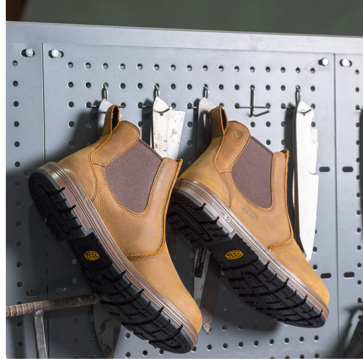  A pair of brown leather, slip-on work boots displayed on a pegboard, emphasizing their functionality in a work environment.