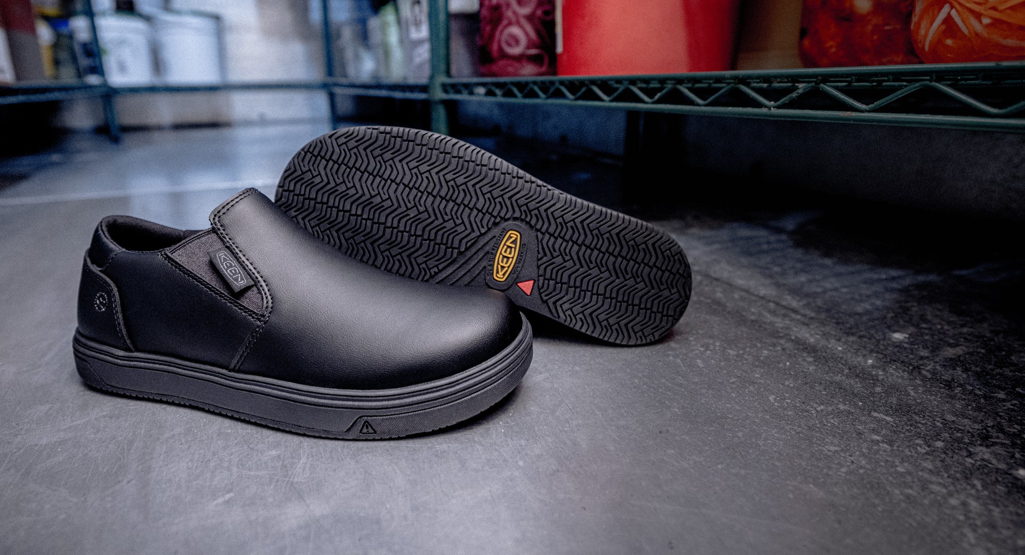 Black slip-on work shoes with non-slip soles resting on a shelf, ideal for workplace safety and comfort.
