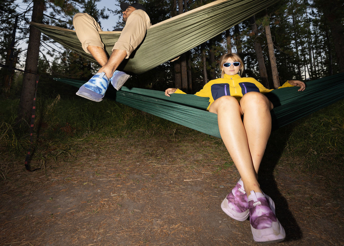 Two people sitting in hammocks, one over the other, at a campsite.