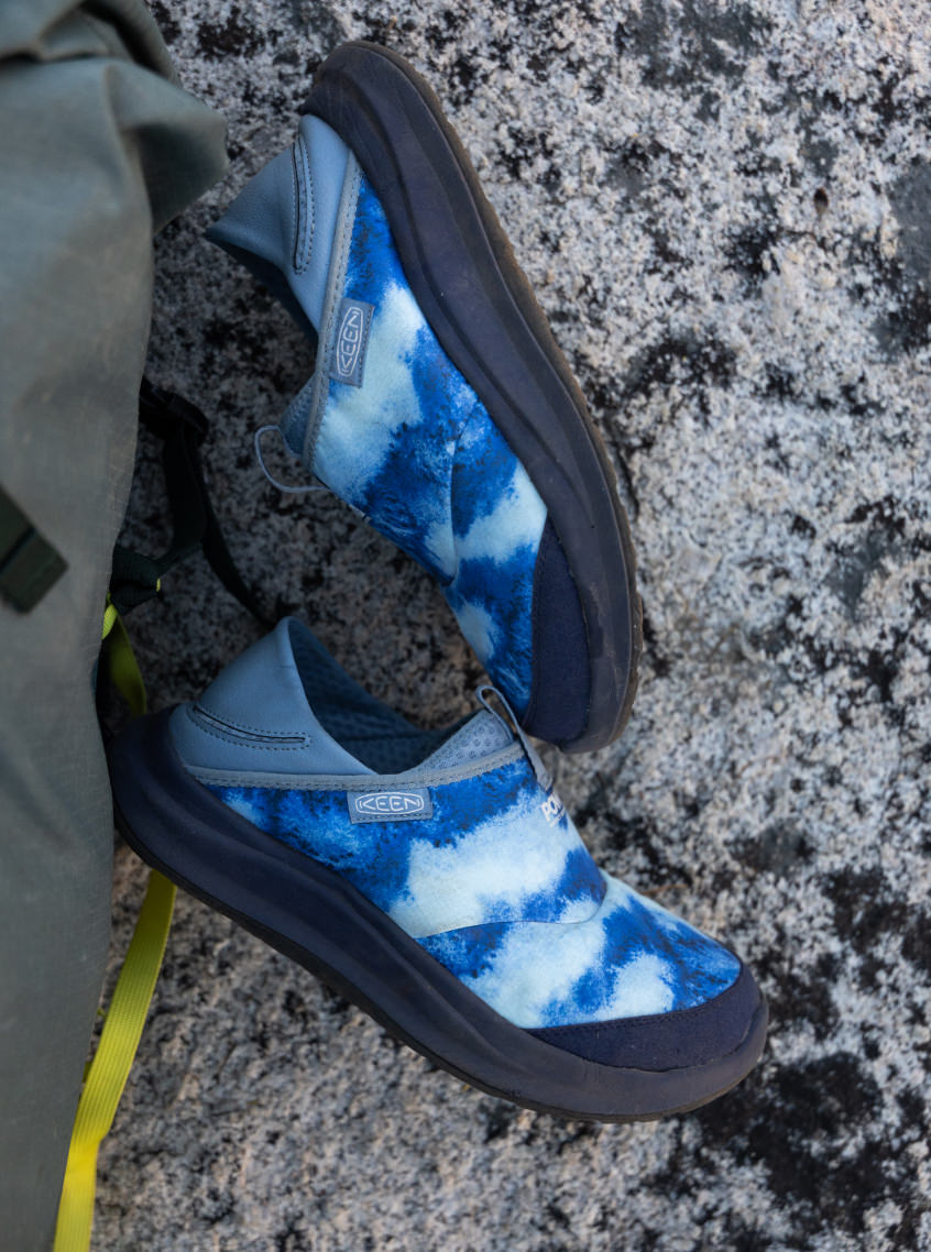 Close up of men's collaboration Whyser shoes laying next to backpack on rock that showcase the blue cushion sole blue gradient design