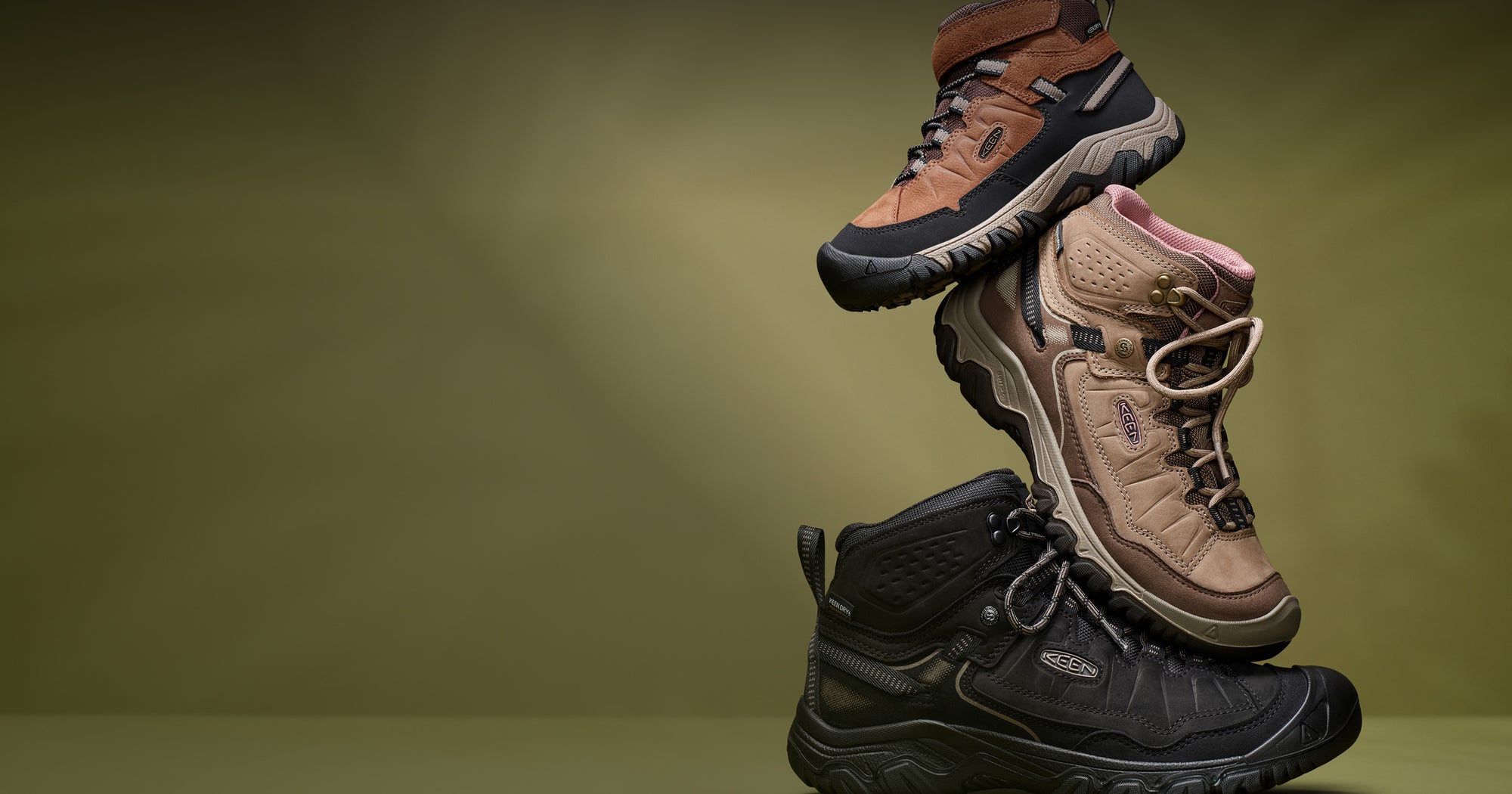 Men's, women's, and kids' hiking boots positioned on a dark green backdrop, showcasing their rugged design suitable for outdoor adventures.