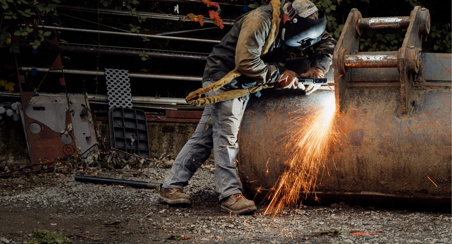 Worker wearing safety gear welding a large metal piece, with sparks flying on a construction site