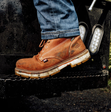 Person wearing worn brown leather work boots with jeans stepping onto a truck platform.