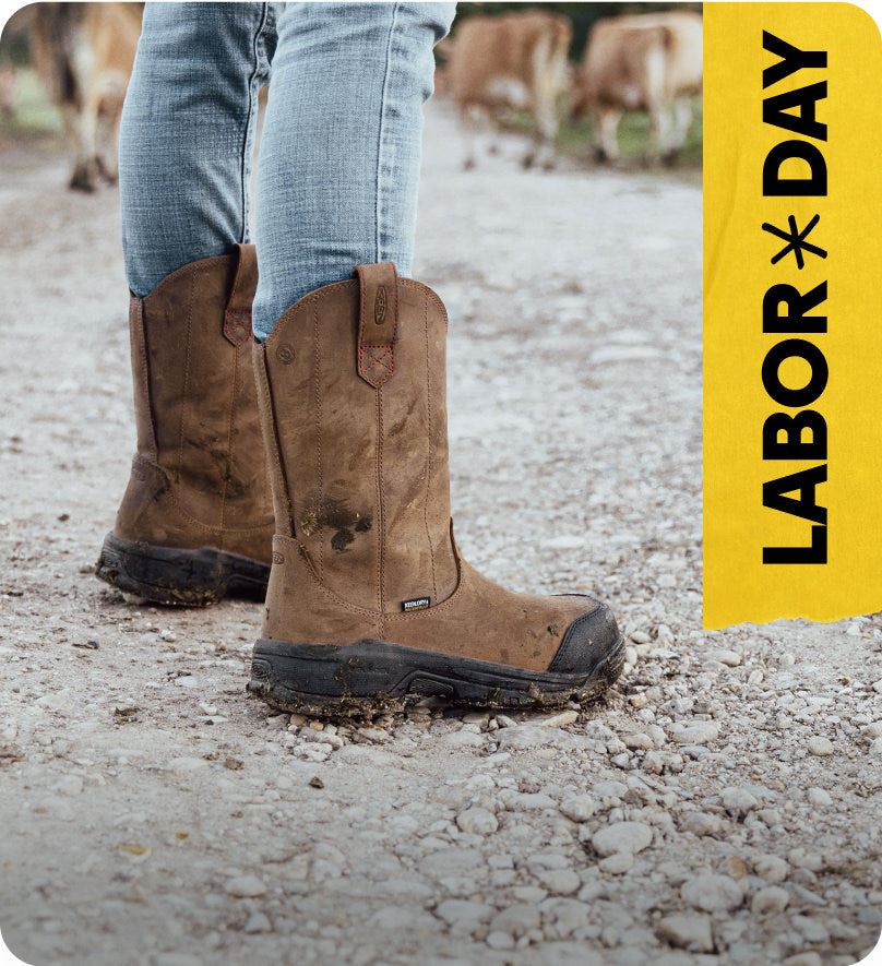 Waist down shot of person in blue jeans wearing pull-on leather work boots and standing on farm landscape. Embedded text reads 