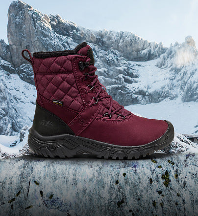 Burgundy quilted winter boot with black sole and laces, shown against a snowy mountain backdrop.