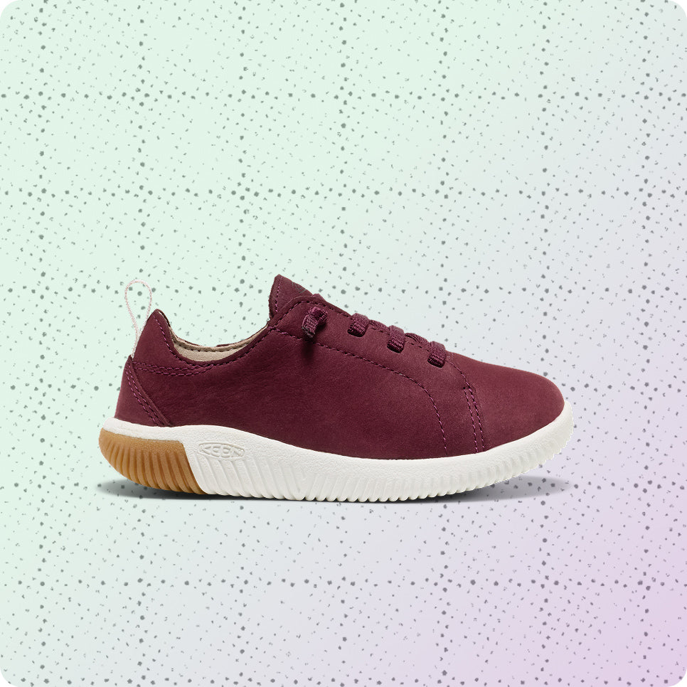 Kids' red leather, lightweight sneaker on a dotted grid wrapping-paper background.