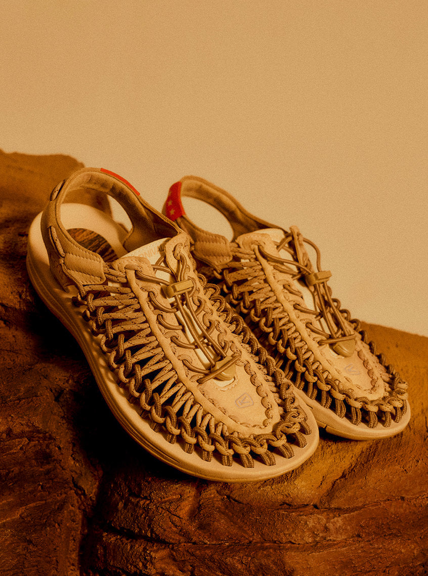 A close-up of off white shoes positioned on a rock, highlighting their natural color and unique string texture in an outdoor setting.