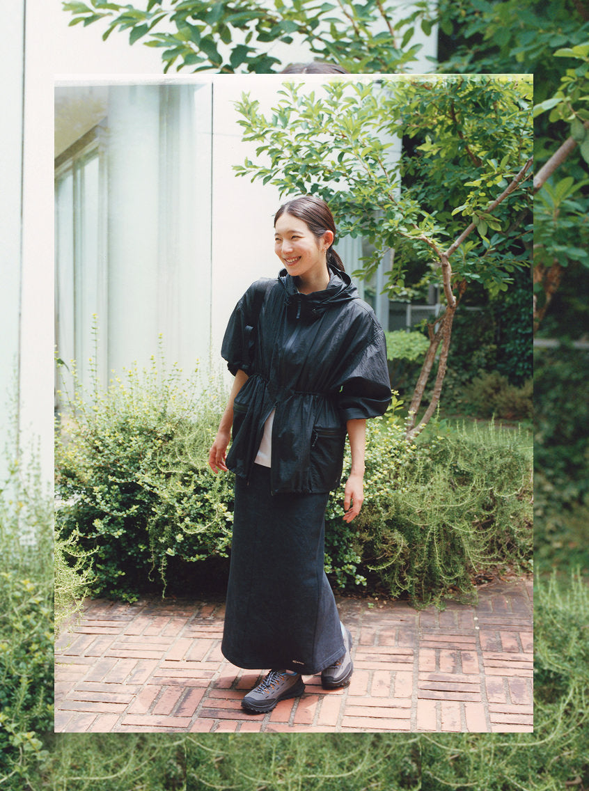 A woman wearing a black jacket and skirt poses in front of a contemporary building sporting modern suede sneakers.