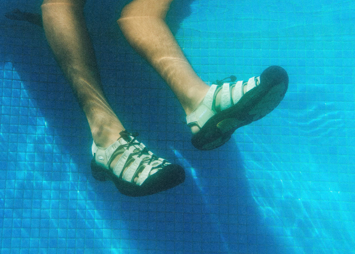 Underwater view of man wearing newport sandals dangling his feet in blue pool water