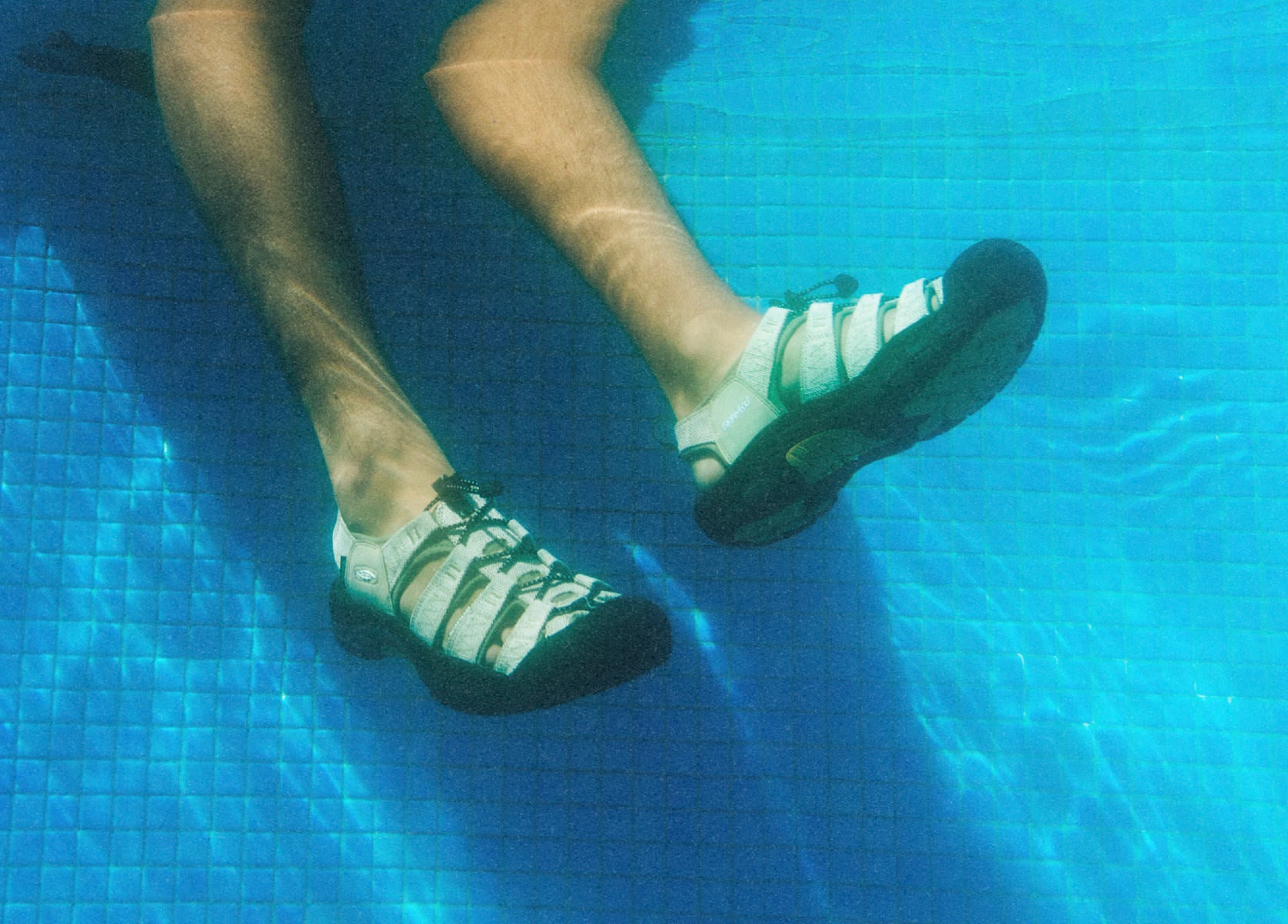 Underwater view of man wearing newport sandals dangling his feet in blue pool water