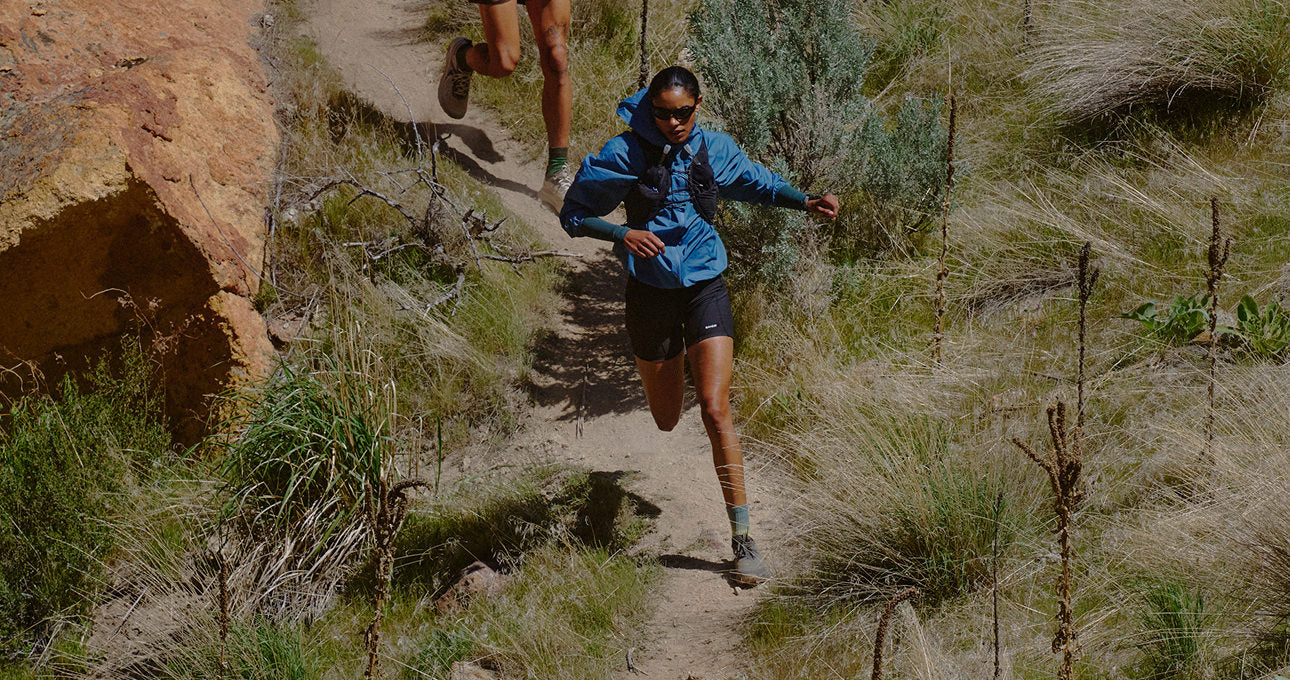Two people running on a high-desert trail, showcasing Roam trail running shoes in a natural outdoor setting.