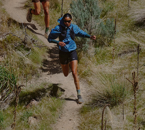 Two people running on a high-desert trail, showcasing Roam trail running shoes in a natural outdoor setting.