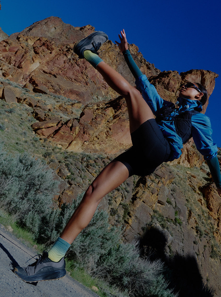 Woman actively stretching while wearing running gear with large mountain the the background. 