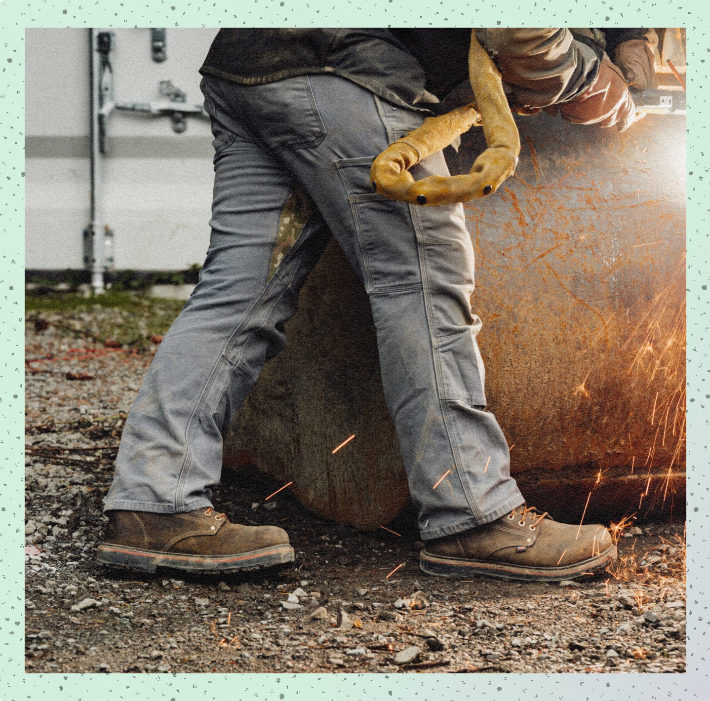 Man using a metal grinder on a large piece of metal while wearing protective leather work boots. 