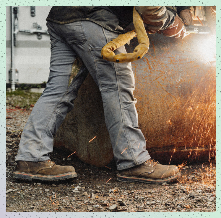 Man using a metal grinder on a large piece of metal while wearing protective leather work boots. 