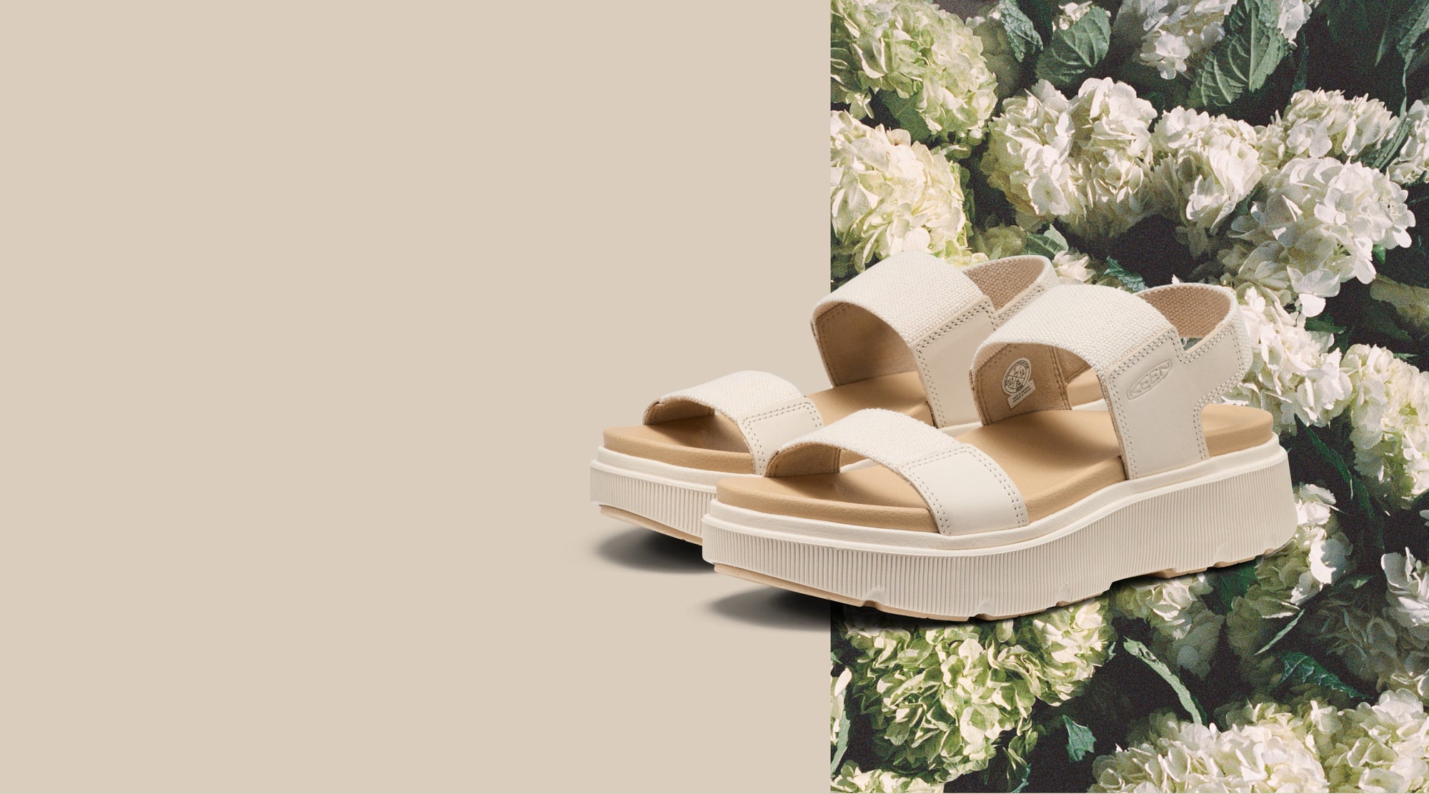 A pair of tan and off-white Elle Mila sandals with white and green hydrangeas in the background.