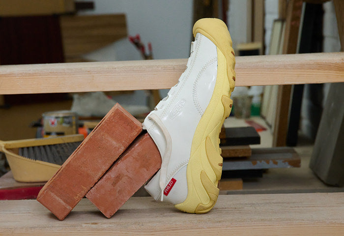 Close up of wooden stairs and two red bricks, one brick is wearing a white KEEN & Phileo collaboration Targher shoe