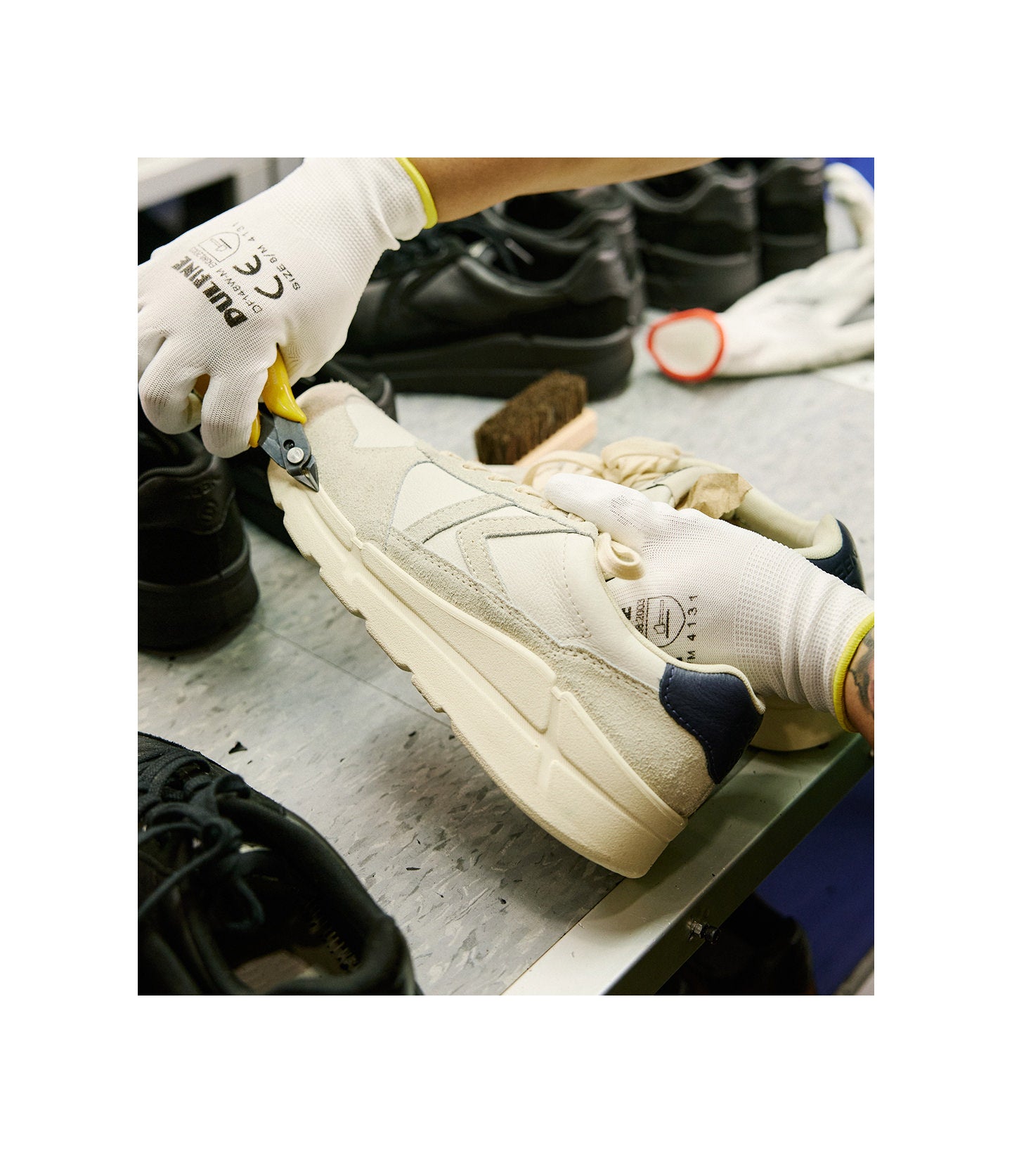 Factory worker wearing white and yellow gloves while working on a pair of KEENmade tan and white leather shoes.