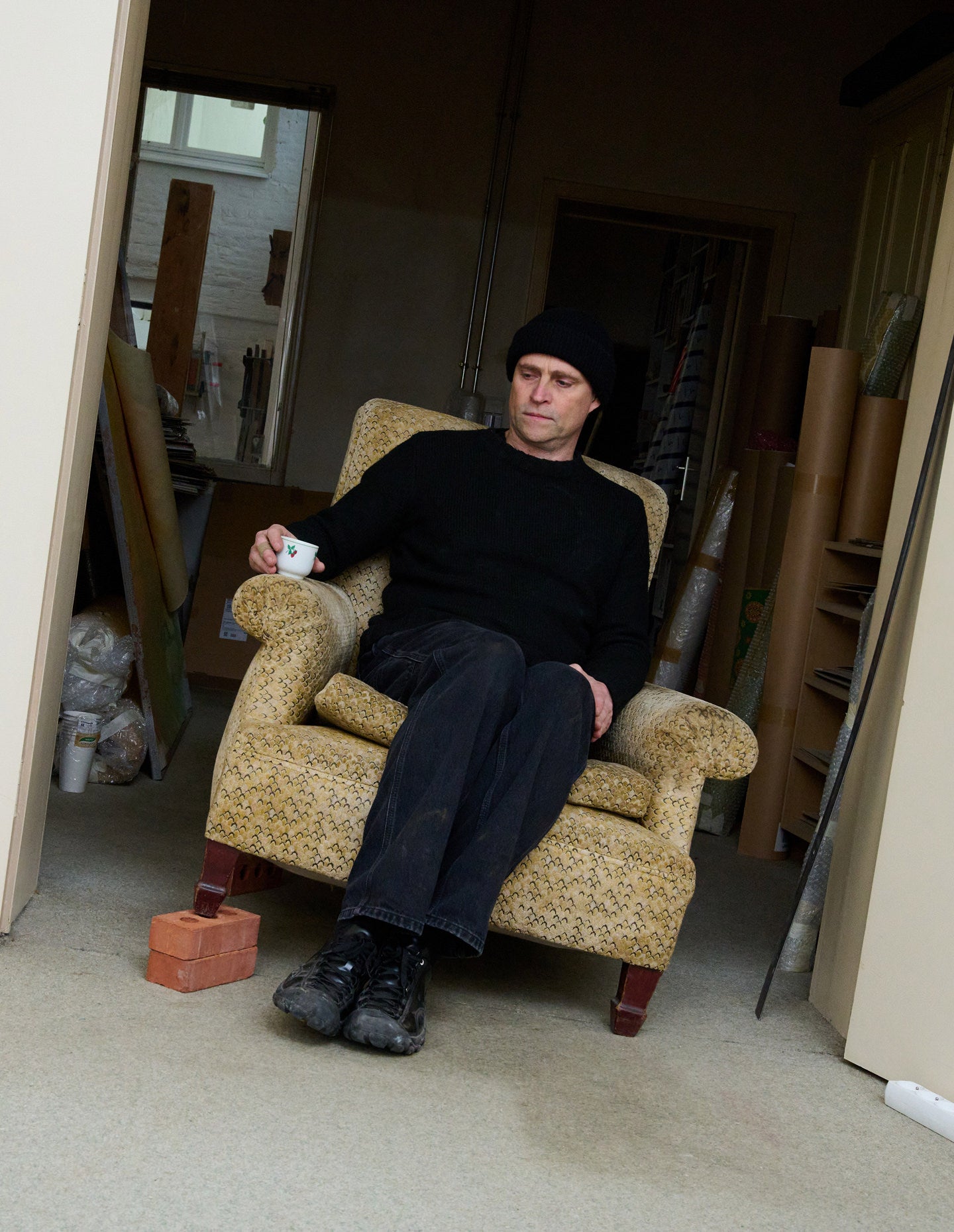 Artist sitting in dusty cushioned chair with espresso cup and wearing black Targher shoes