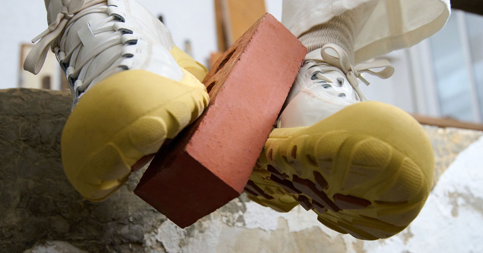 Person lifting a red brick between feet wearing White Targher Collaboration shoes. 