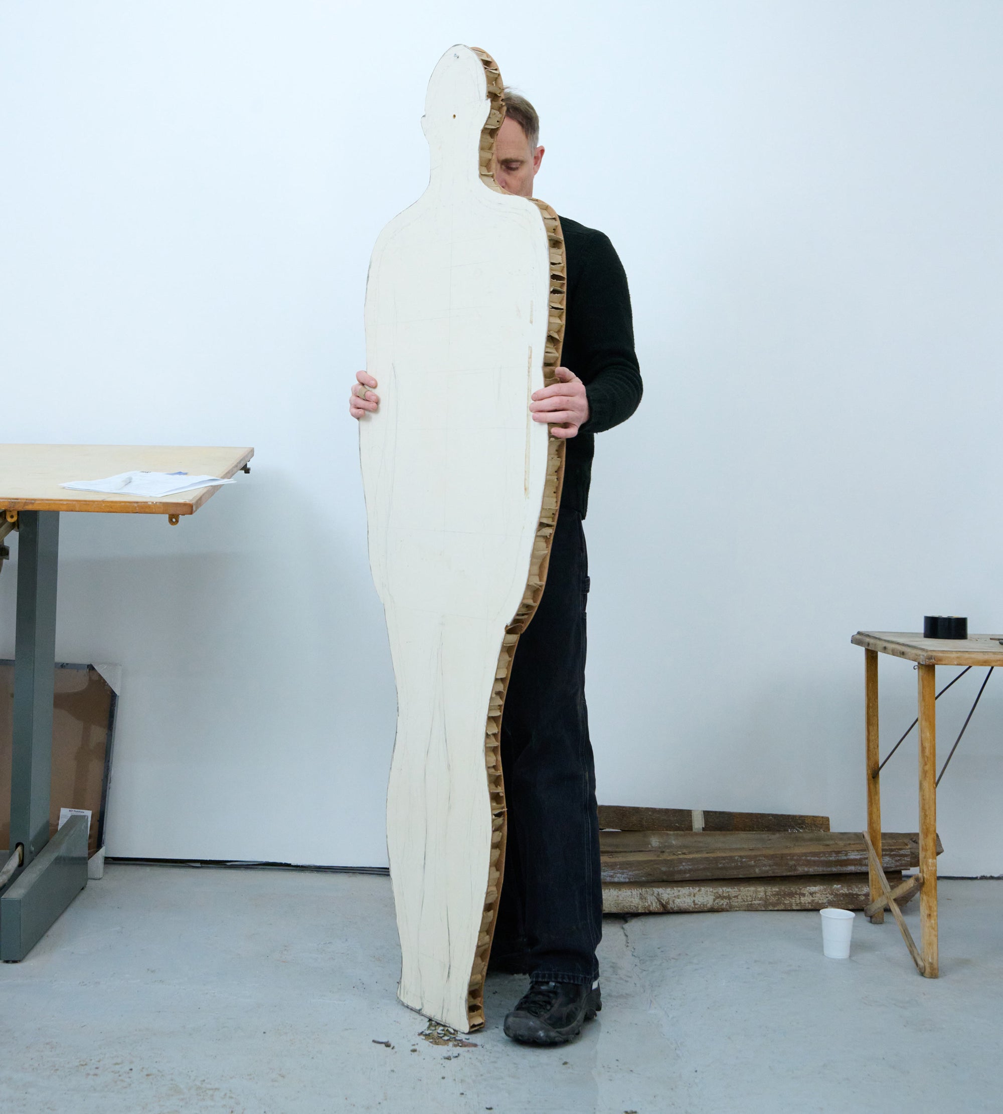 Artist wearing black Targher shoe positions human shaped cutout in studio space.