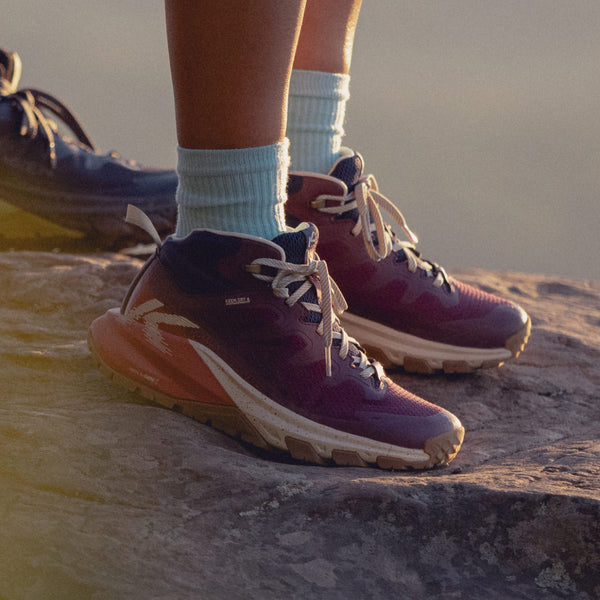 Knee-down shot of woman standing on a rock and wearing the Targhee Apex hiking boots in purple, blue and pink. 