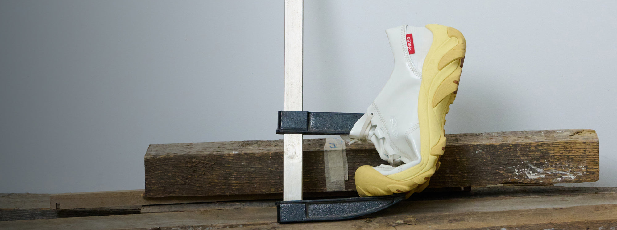 White and yellow Philo collaboration Targher sneaker pressed between a metal clamp on a woodworking station. 