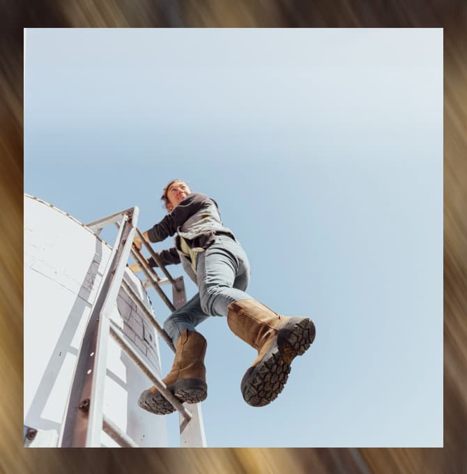 A woman climbing a ladder while wearing the brown Evanston pull-on waterproof work boot, showcasing the ultra tough tread and protective outsole.