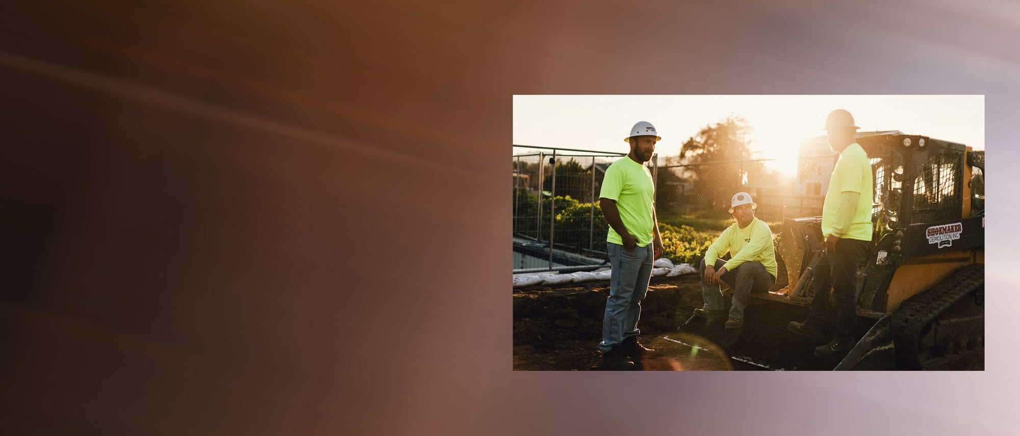 Three construction workers in yellow shirts and white protective helmets standing around a tractor at sunset while wearing a variety of KEEN work boots. 