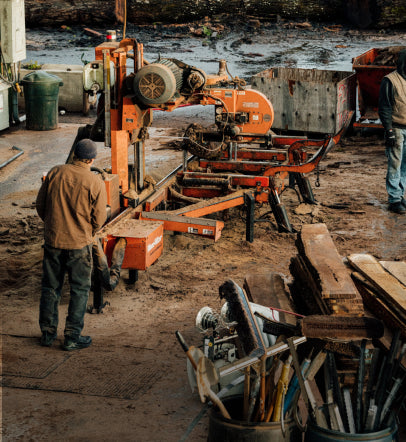 Two tradesmen working with a large wood pressing machine in a lumberyard. 