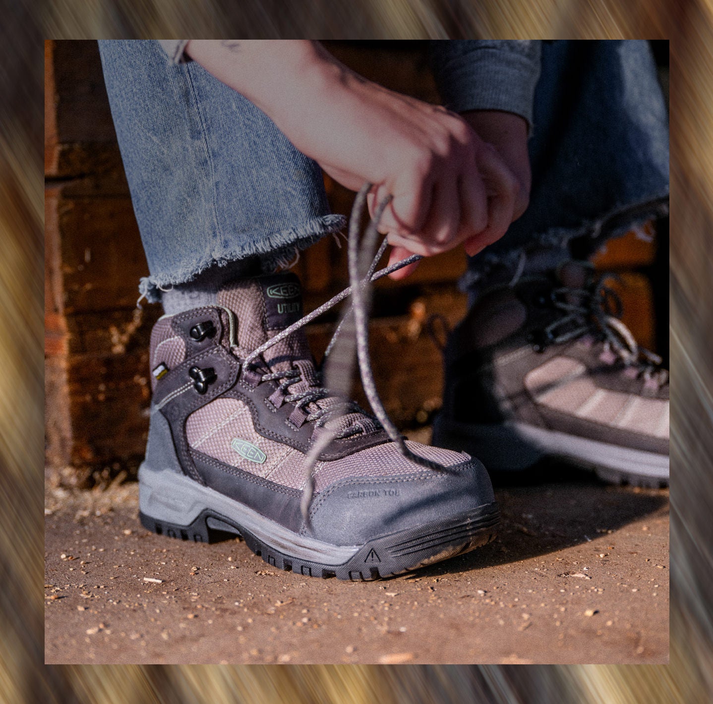 A woman sitting on a wood block lacing up her grey, waterproof Skokie work boots with a hiking-boot aesthetic and carbon toe. 