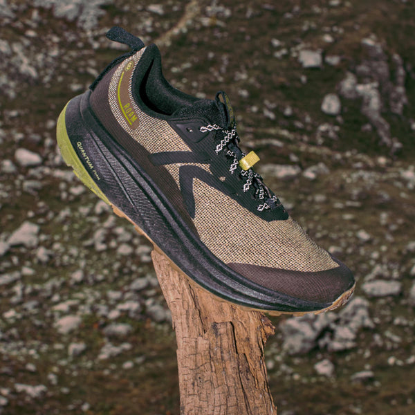 A single Men's Roam running shoe in Dark Olive and Golden Cypress sitting on a tree branch with a rocky valley below. 