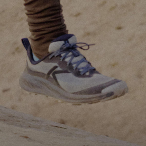Close up shot of woman in brown running leggings and Indigo and light blue Wander trail running shoes. 