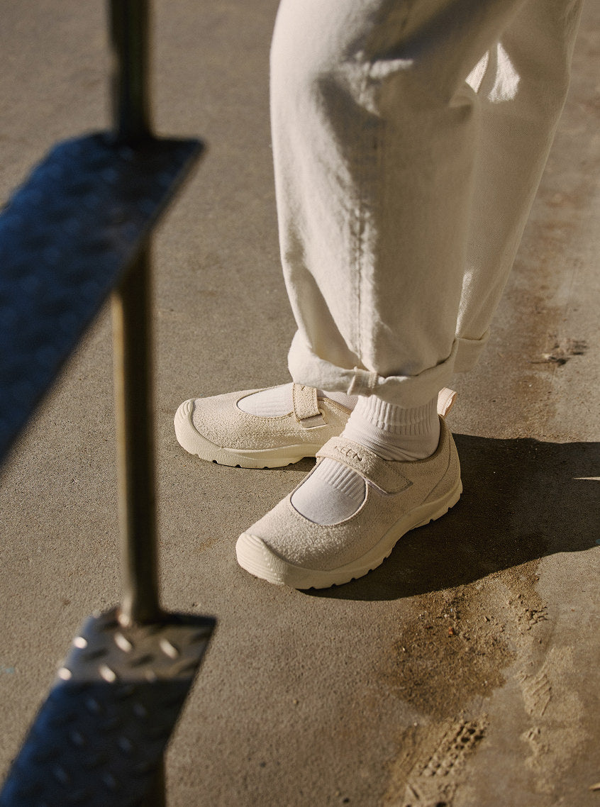 A woman in cream pants and white socks standing on pavement while wearing the KM Lite Mary Jane sneakers. 