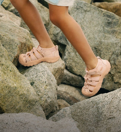 Child in KEEN newport sandals climbing up boulders.