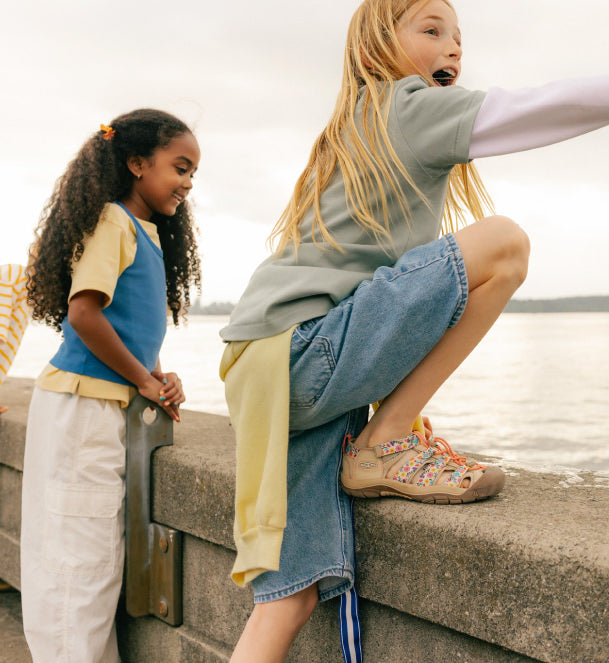 Two kids looking over a sea wall wearing KEEN closed toe sandals. 