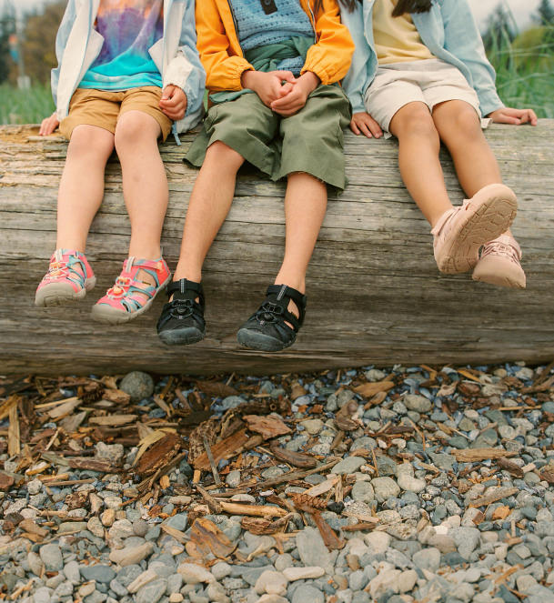 Three kids sitting on a log by a river wearing keen Seacamp CNX II and Newport H2 closed toe sandals.
