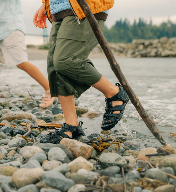 Two kids walking along a rocky river bank wearing keen closed toe sandals 