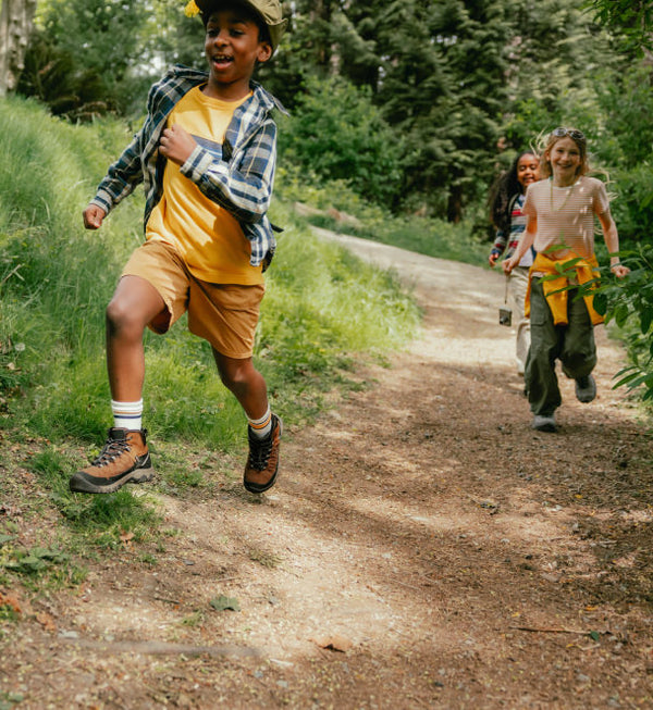Three kids running down a forest path wearing keen kids boots.