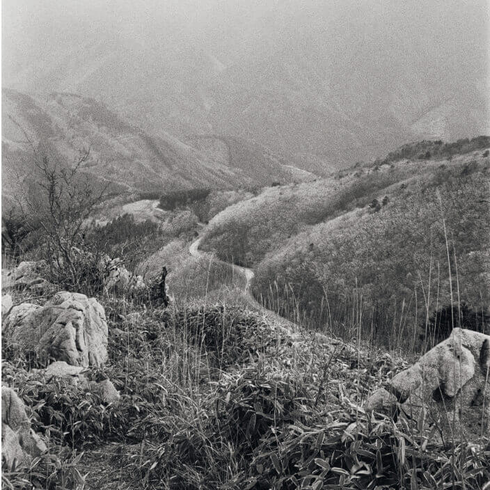 Black and white landscape image of mountain trail weaving into the distant valley canyon