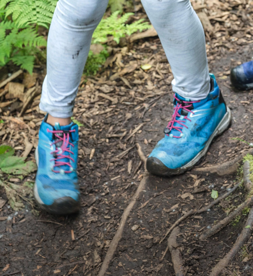 Knee down shot of girl in gray leggings and blue Wanduro boots walking on dirt path. 