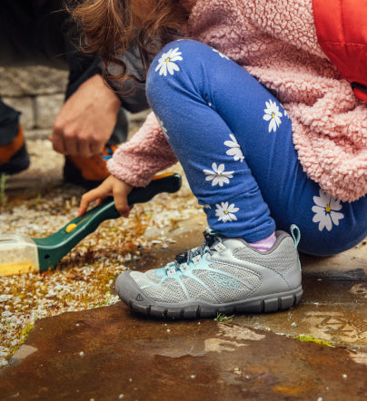 Little girl in floral leggings wearing gray Chandler 2 CNX shoes and playing in sandbox