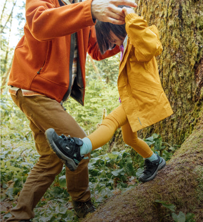 Dad helping a little girl jump off tree branch while wearing Targhee shoes